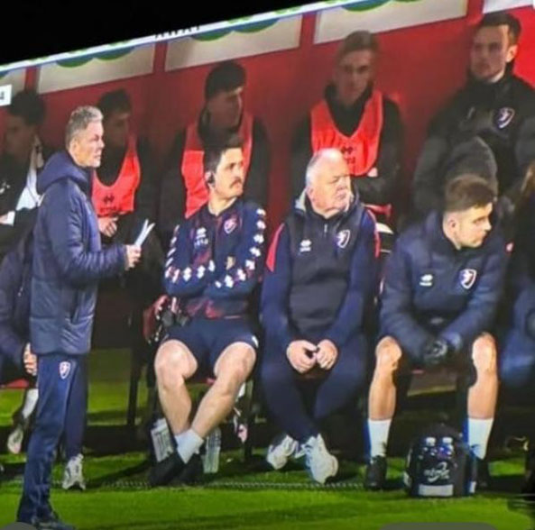 Gerry Oldham, seated, second from the right, in the Cheltenham Town dugout last night