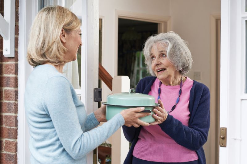 Kind woman taking food to elderly neighbour