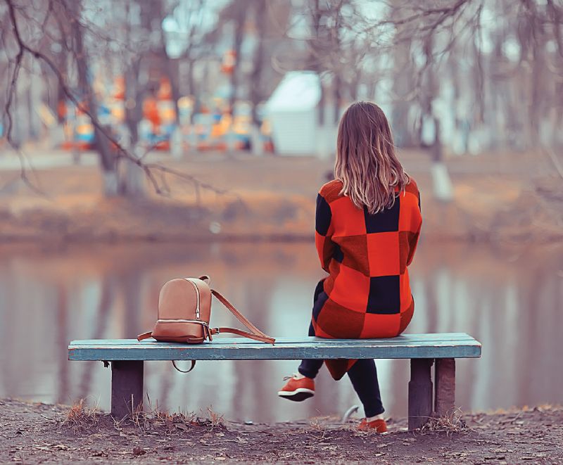 Sad lonely woman sat on bench autumn lake
